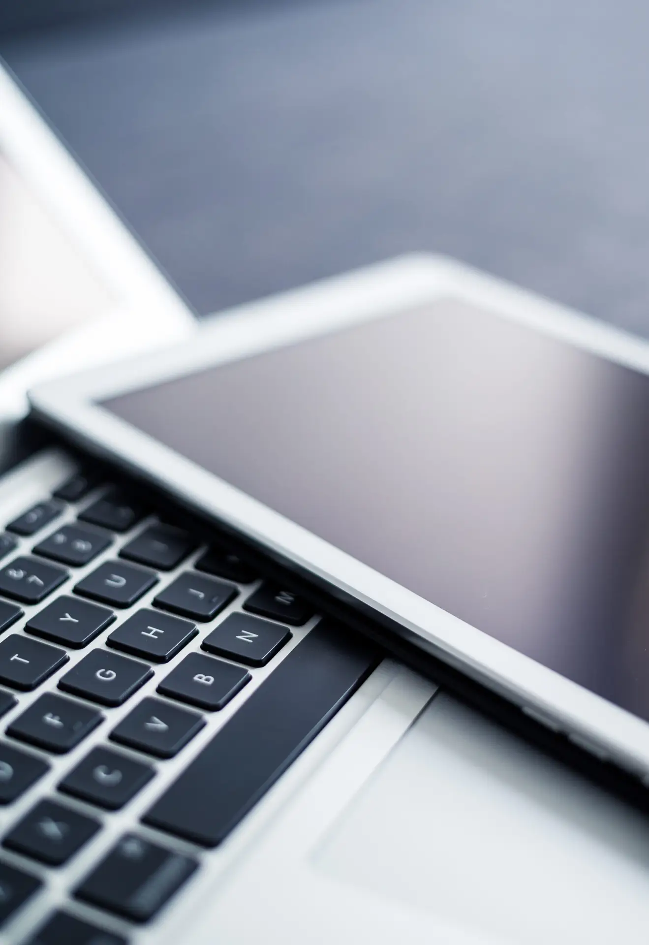 Close-up of a laptop keyboard and a tablet on a desk